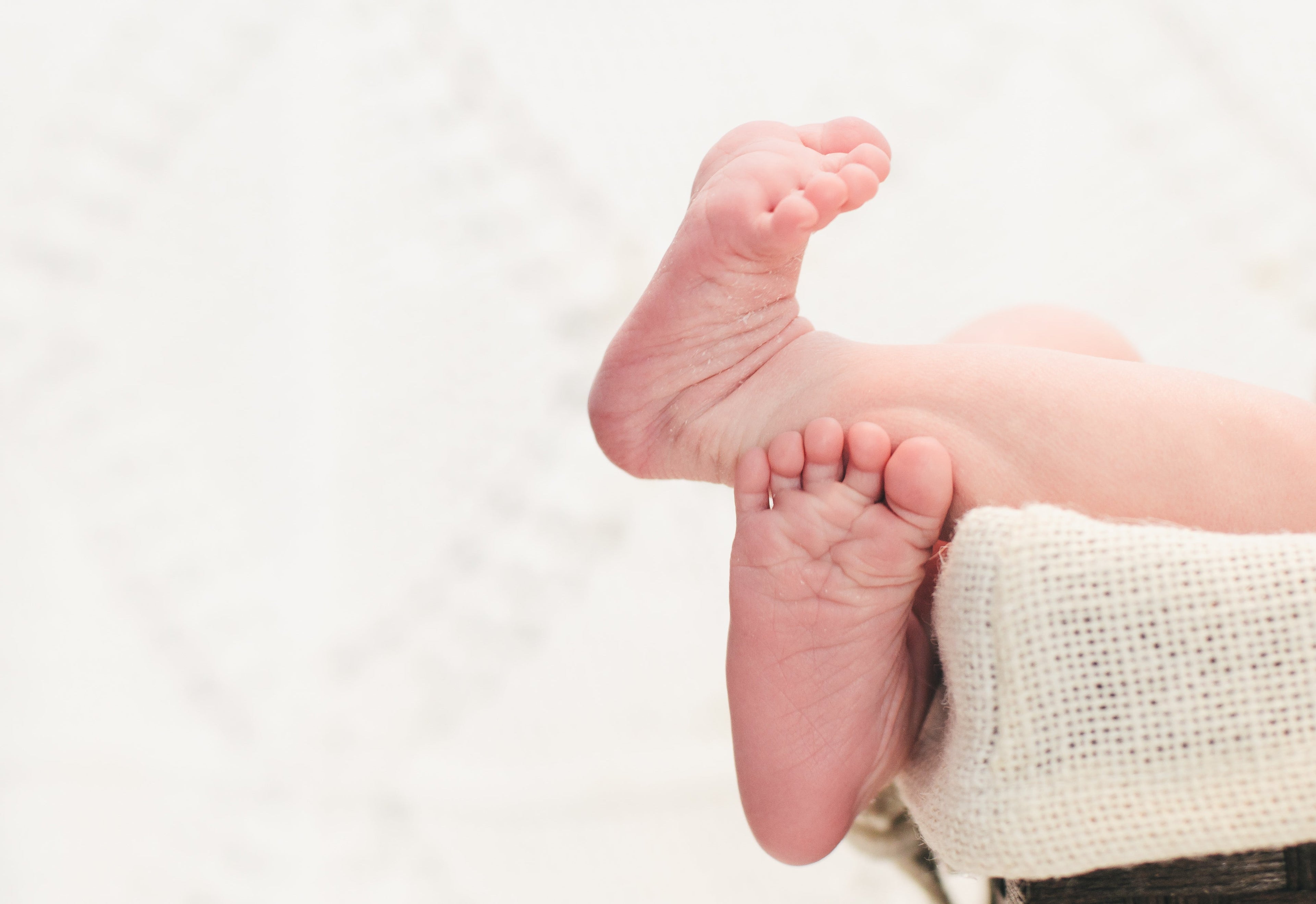 newborn baby feet hanging of baby basket covered with soft ivory burlap cloth