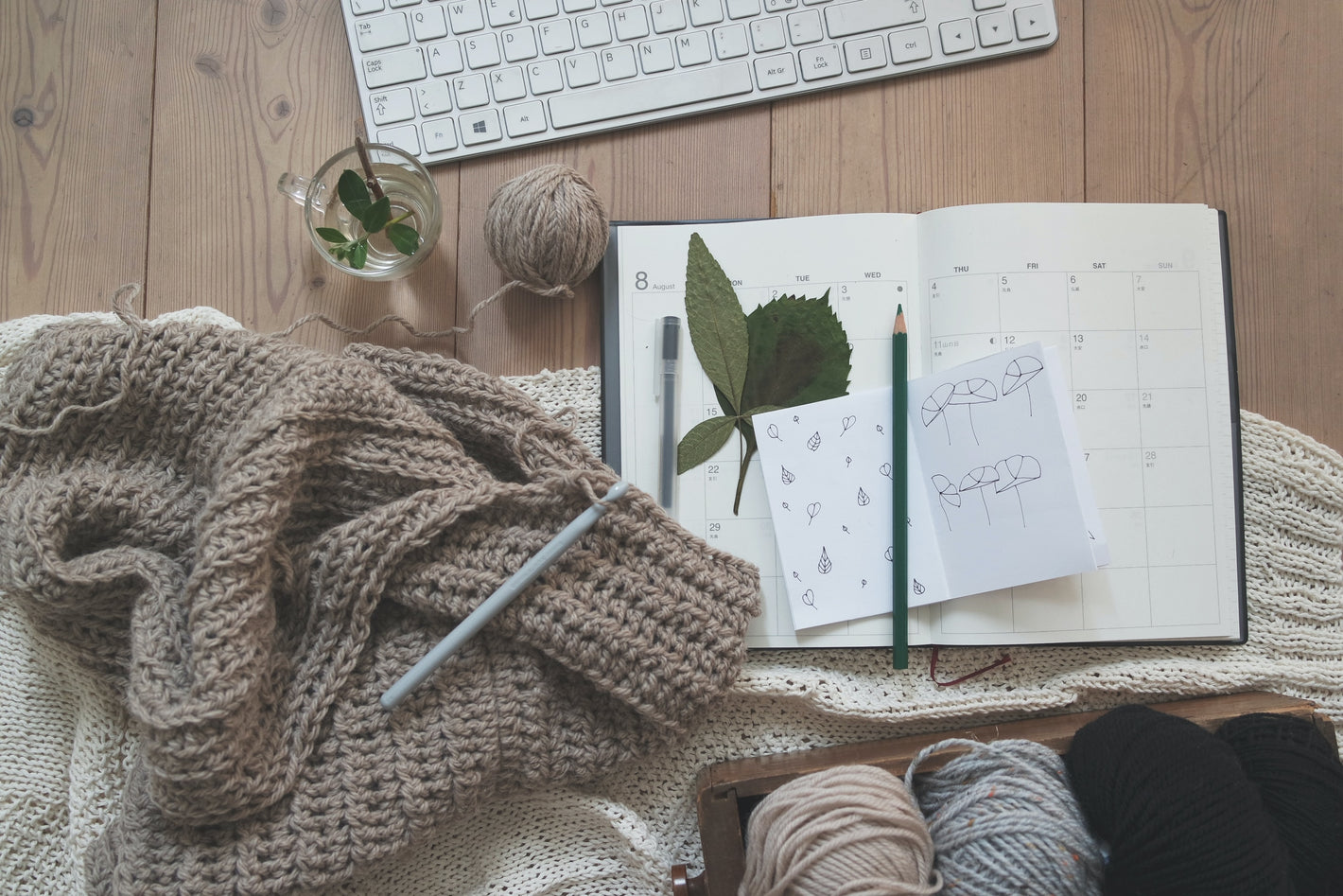 Yarn, crochet work in progress, crochet hook, planner, pencil, and keyboard on the background